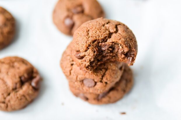 Close-up of three 3 stacked Paleo Double Chocolate Fudge Cookies on a parchment paper-lined tray with more cookies in the background.