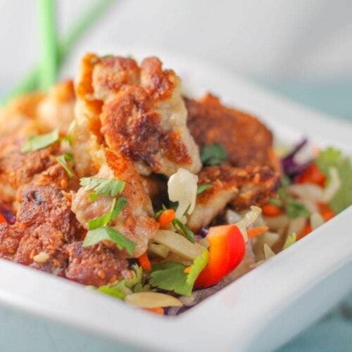 Paleo Sesame Chicken served on chopped Asian vegetables in a white bowl.