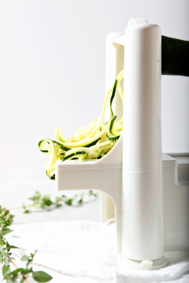 side view of zucchini being cut into zucchini noodles with a spiralizer