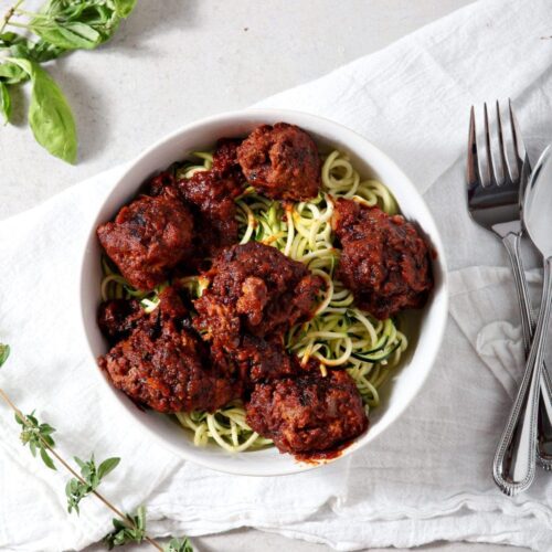 Whole30 Spaghetti and Meatballs served over zucchini noodles in a white bowl on a white tablecloth.