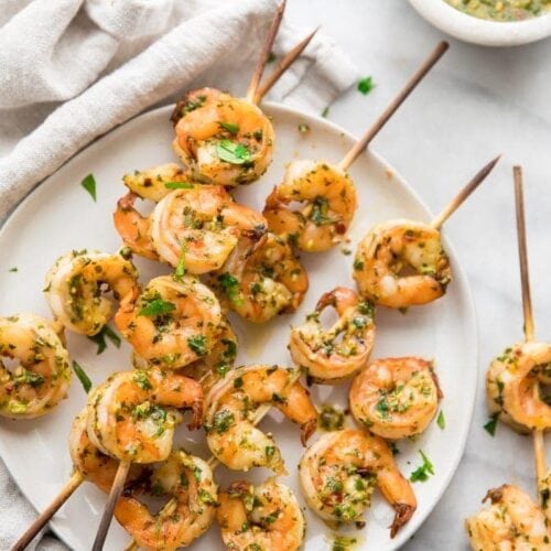 Quick Whole30 chimichurri shrimp skewers on a plate with a bowl of chimichurri