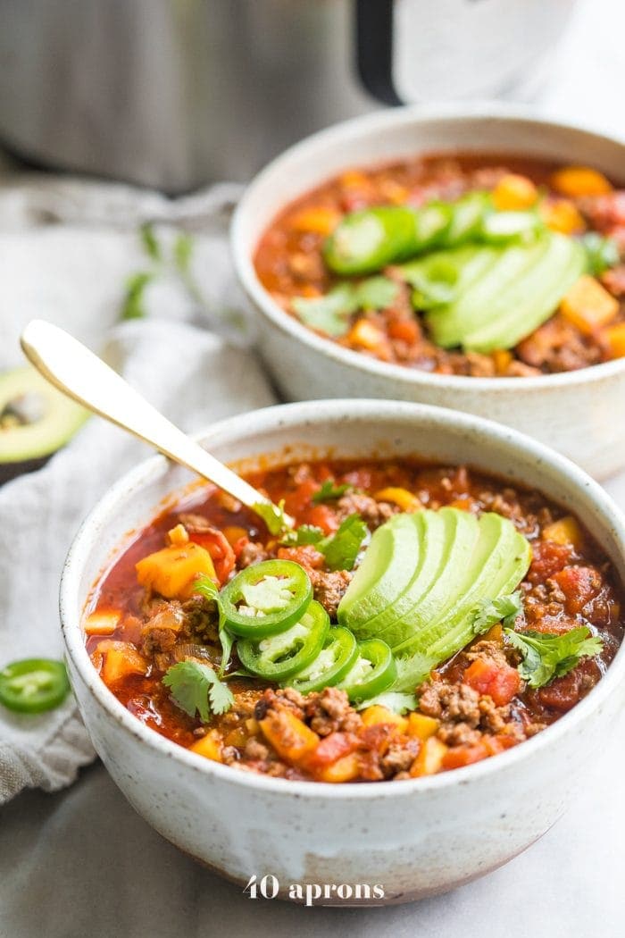 Two bowls of Instant Pot Whole30 chili with butternut squash topped with jalapenos and avocados with Instant Pot in background