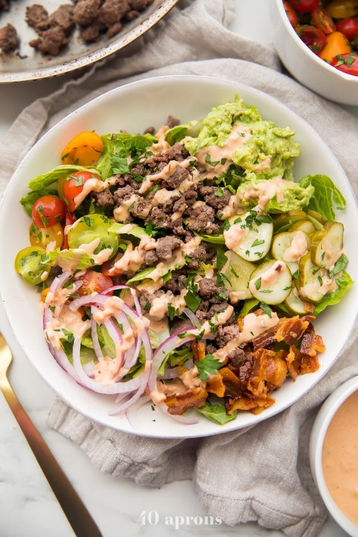 Overhead shot of Whole30 loaded burger bowls with ground beef, red onions, bacon, pickles, guacamole, and tomatoes