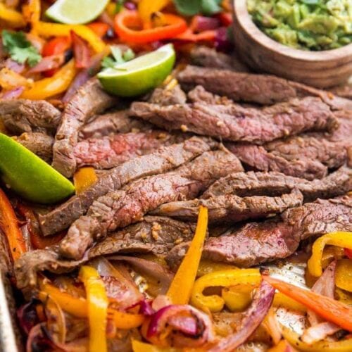 Best sheet pan fajitas with steak and peppers on a sheet pan with lime slices and guacamole off to the side