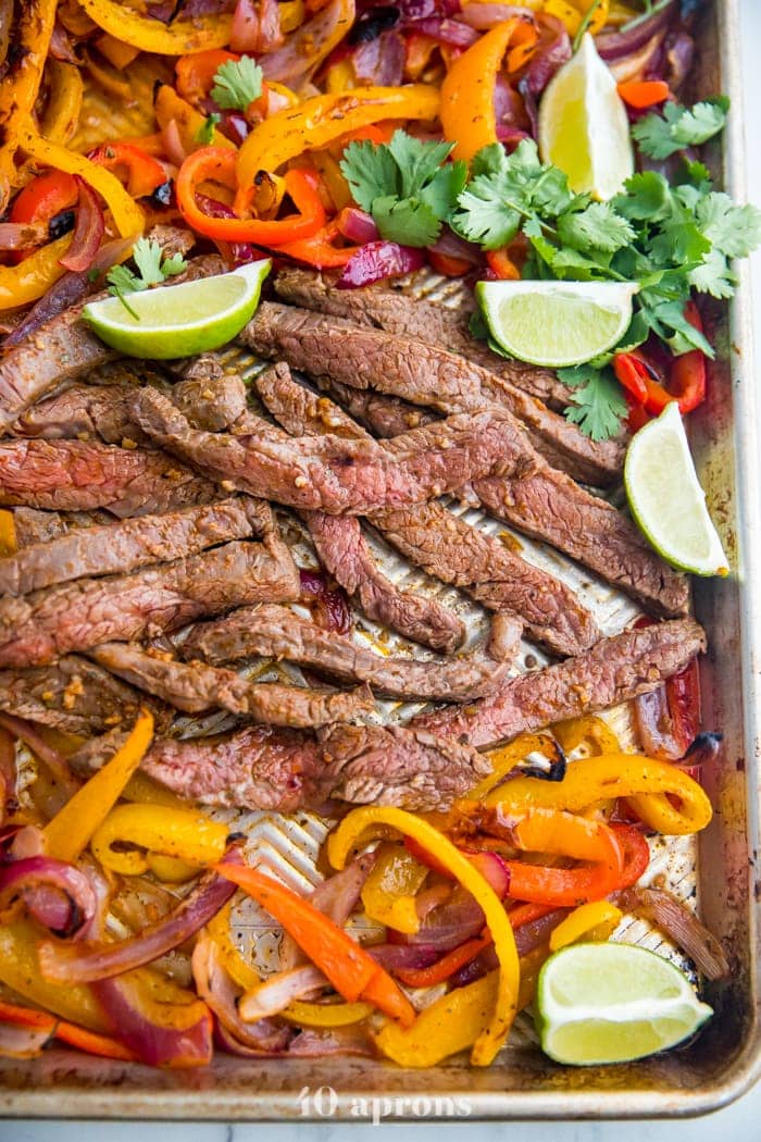 Best sheet pan fajitas with steak and peppers on a sheet pan with lime slices and guacamole off to the side