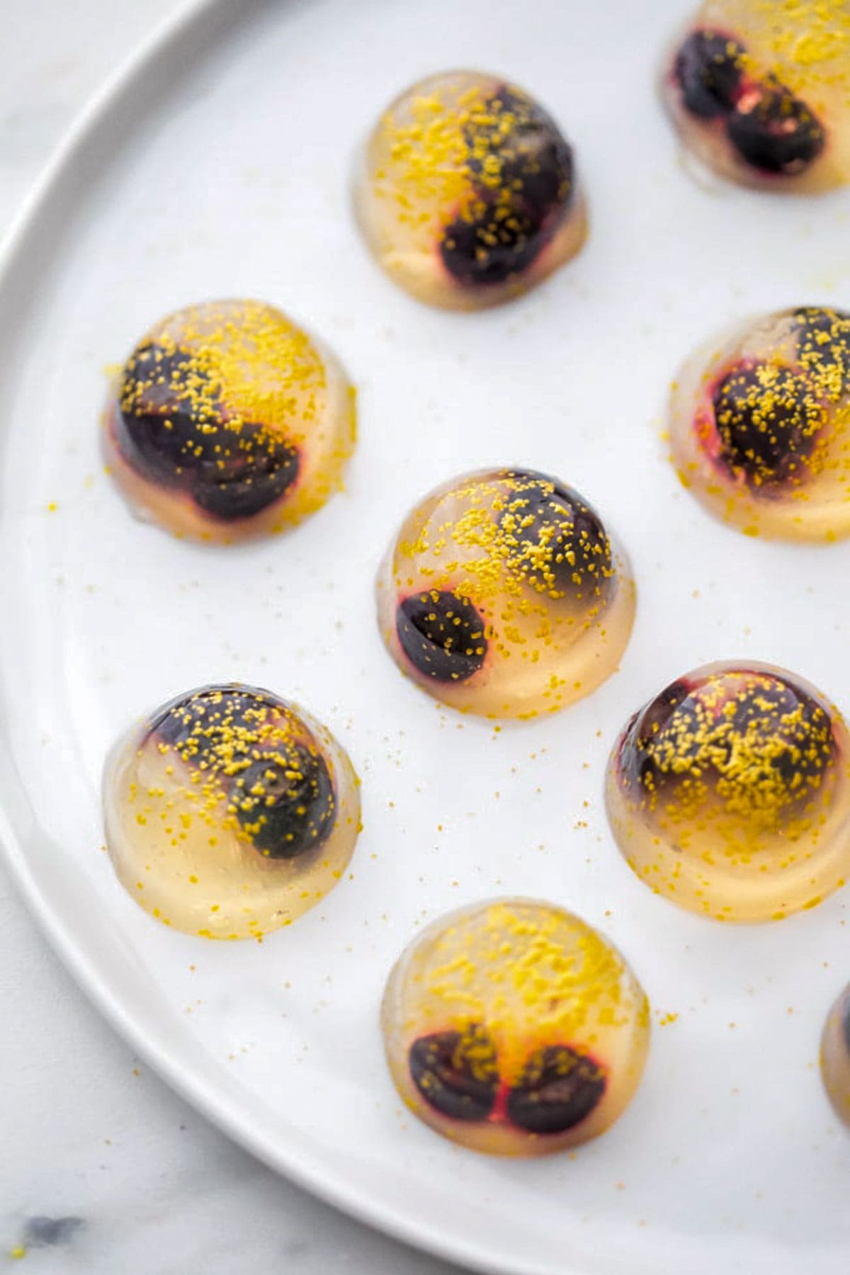 Top-down view of several jello shots with champagne, blueberries, and gold sanding sugar on a plate.