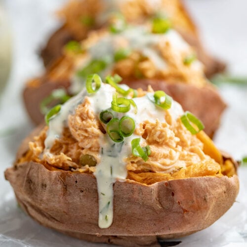 Buffalo chicken stuffed sweet potatoes topped with ranch dressing and green onions.