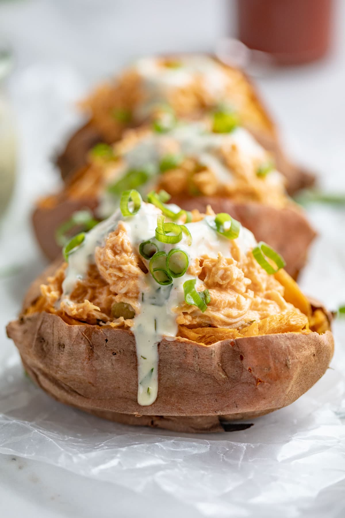 Buffalo chicken stuffed sweet potatoes topped with ranch dressing and green onions.