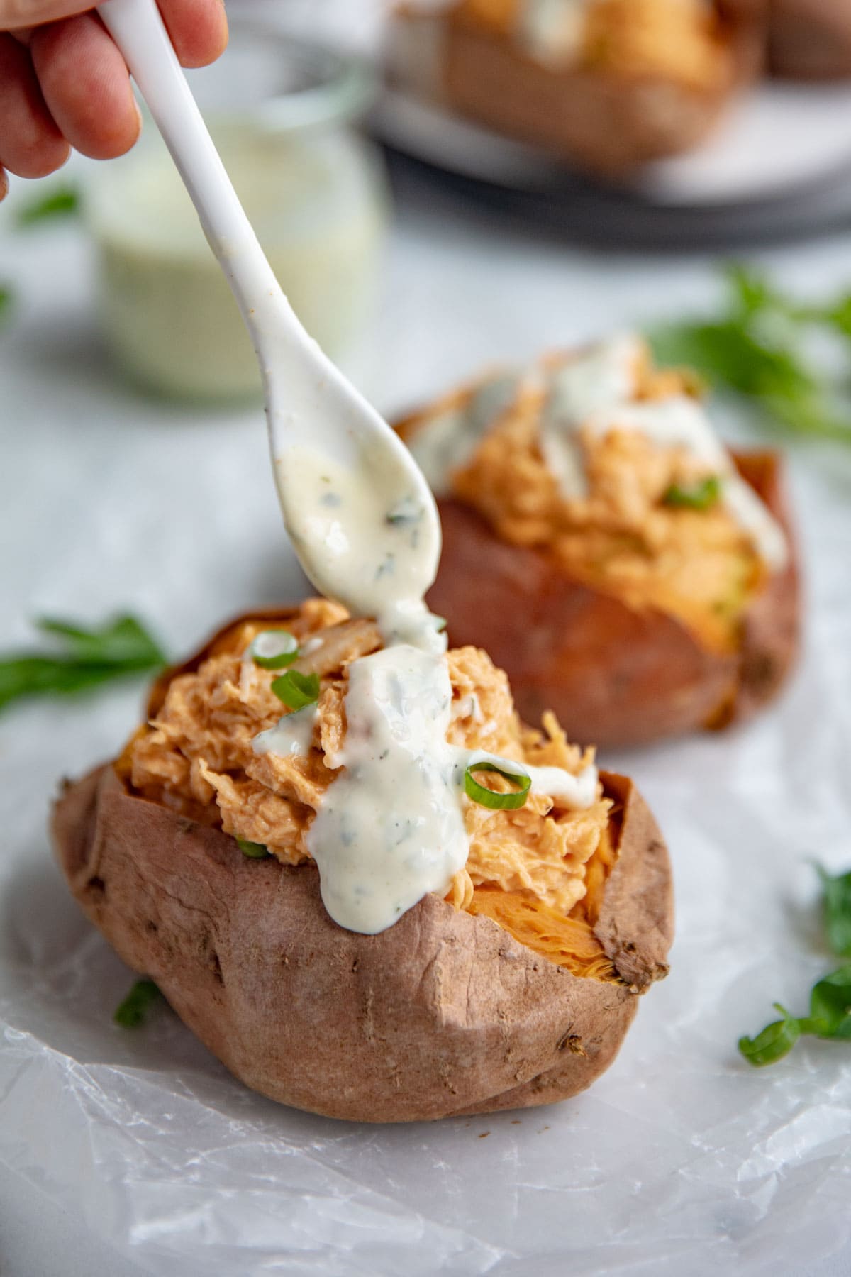 Buffalo chicken stuffed sweet potatoes topped with ranch dressing and green onions.