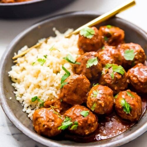 Indian meatballs with creamy sauce next to cauliflower rice topped with cilantro in a grey dish