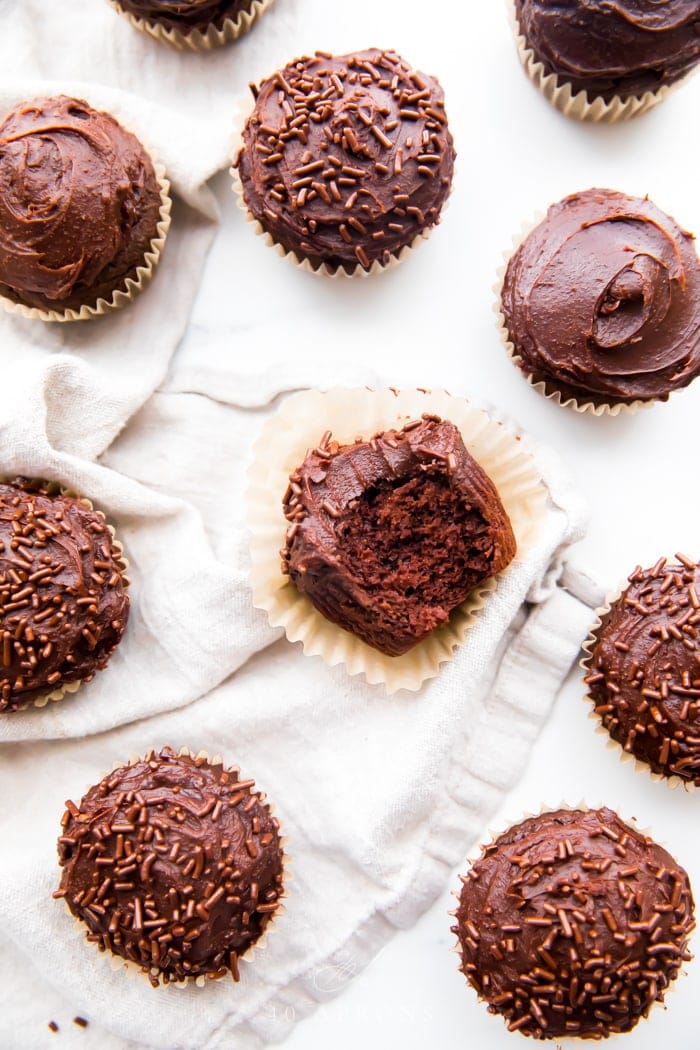 Overhead shot of many chocolate paleo cupcakes frosted with dark chocolate frosting and one bite taken out of one