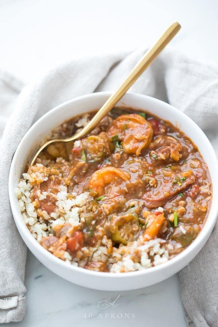 Healthy authentic seafood gumbo in a bowl with shhrimp and okra over cauliflower rice in a white bowl with gold spoon