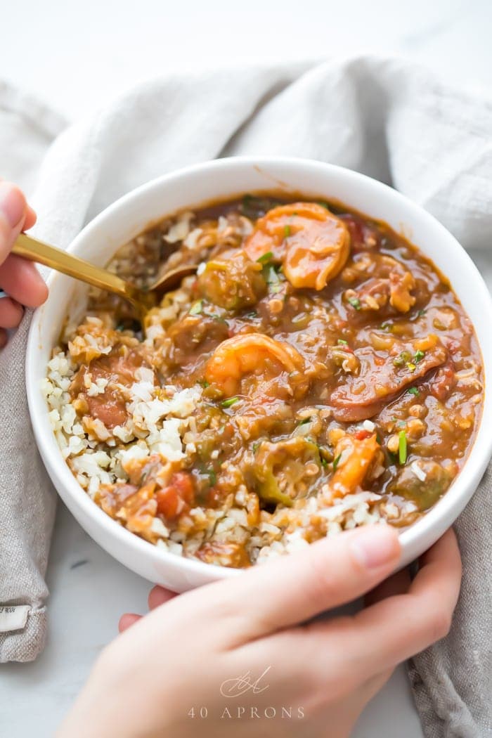 Hands holding a bowl of healthy authentic seafood gumbo with a white spoon