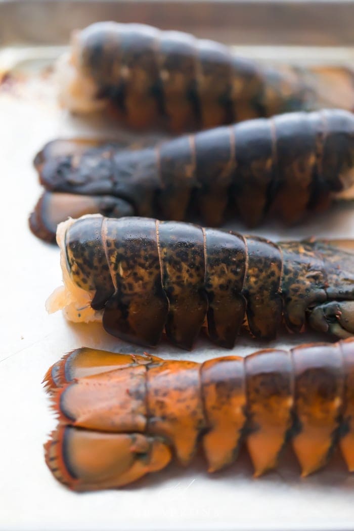 Four uncooked lobster tails on a baking sheet