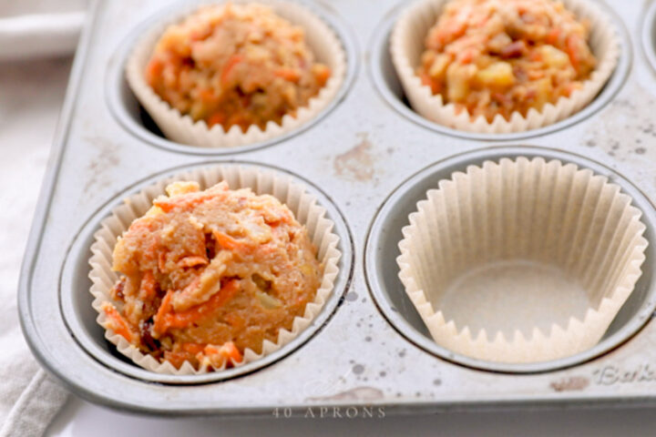 3 cupcake liners filled with carrot cake cupcake batter. A 4th, empty cupcake liner waits to be filled.