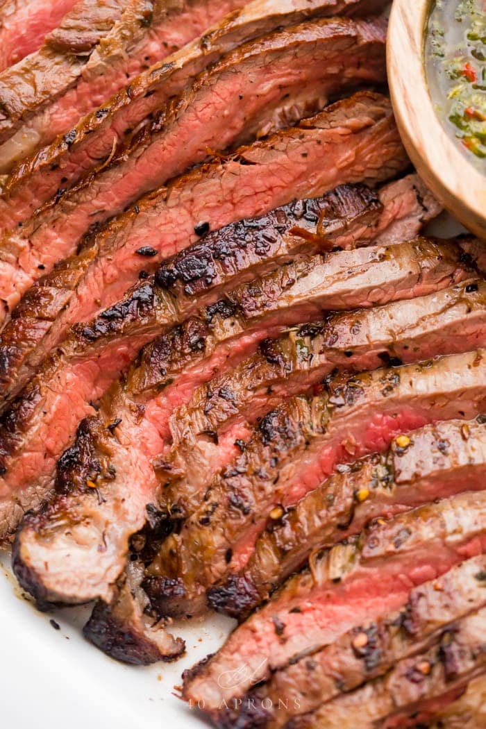 Medium rare sliced flank steak with a bowl of chimichurri sauce