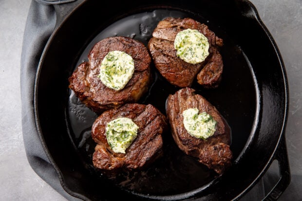 4 filet mignon topped with a compound butter in a cast iron skillet