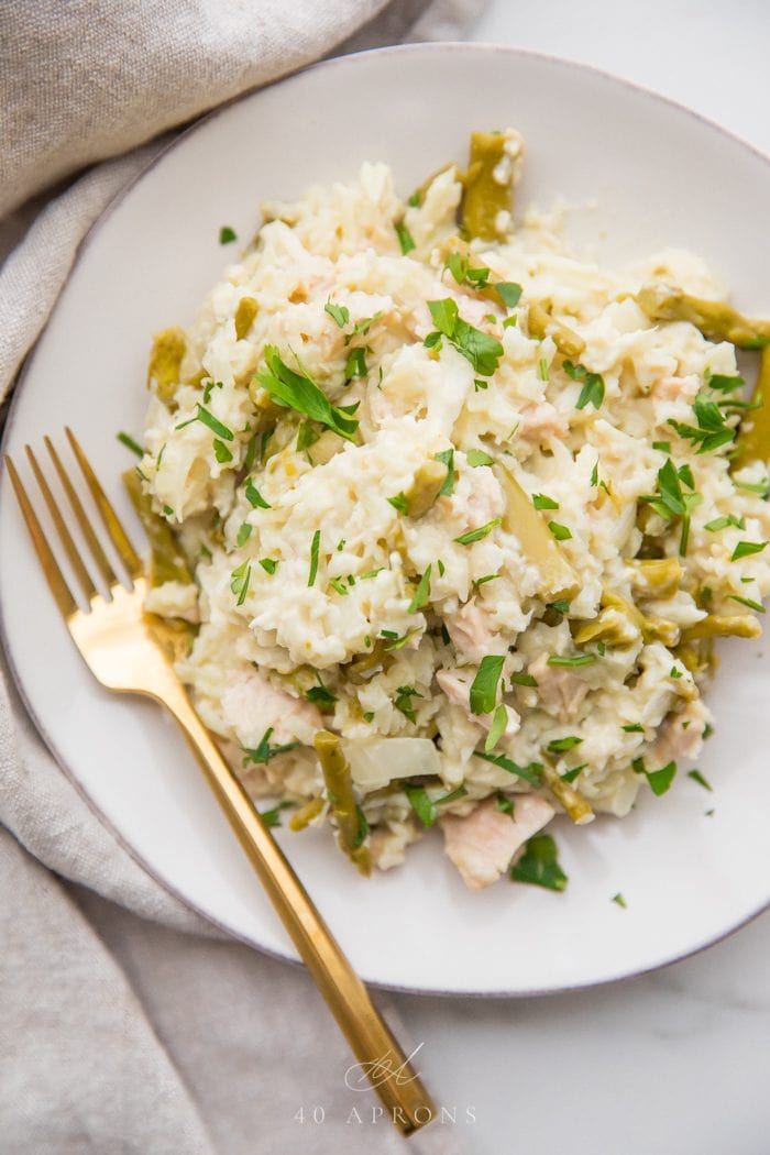 Quick creamy Whole30 cauliflower risotto with chicken and asparagus on a white plate with a gold fork, grey linen napkin next to the plate