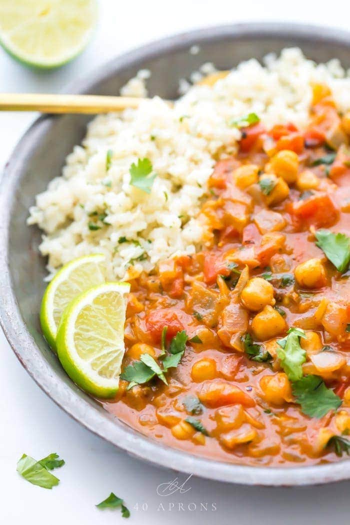 Creamy vegan coconut curry over cauliflower rice in a bowl with lime slices