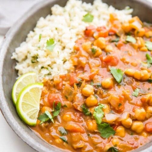 Creamy vegan coconut curry over cauliflower rice in a bowl with lime slices