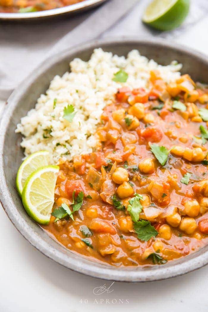 Creamy vegan coconut curry over cauliflower rice in a bowl with lime slices