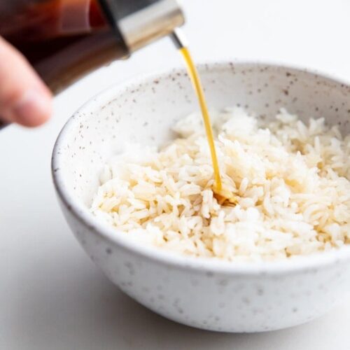 A bottle of soy sauce substitute pouring over a bowl of white rice