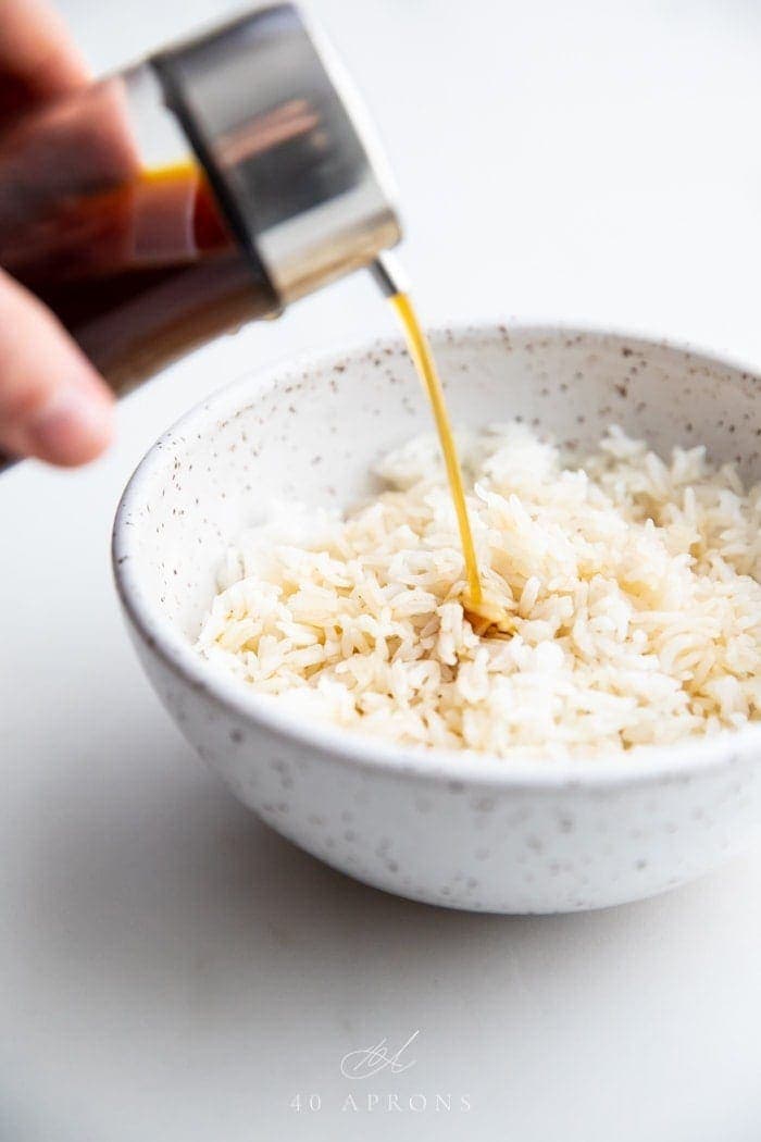 A bottle of soy sauce substitute pouring over a bowl of white rice