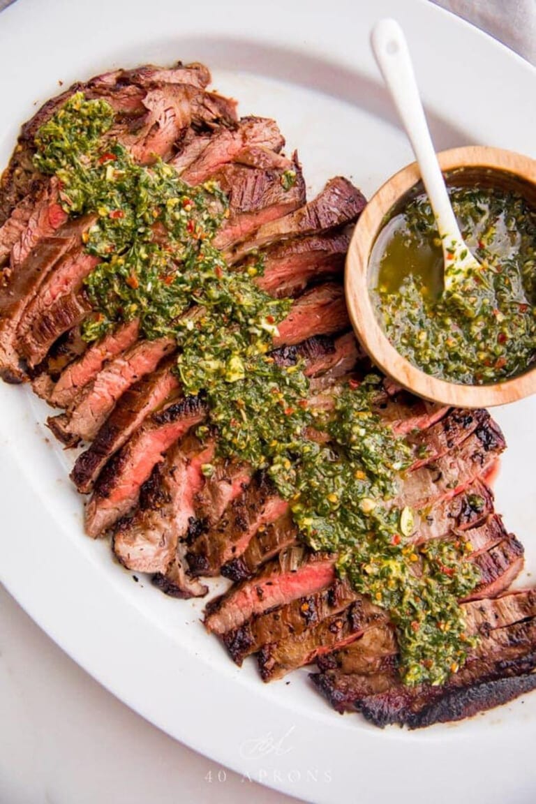 Overhead view of a platter of sliced flank steak coated in chimichurri.