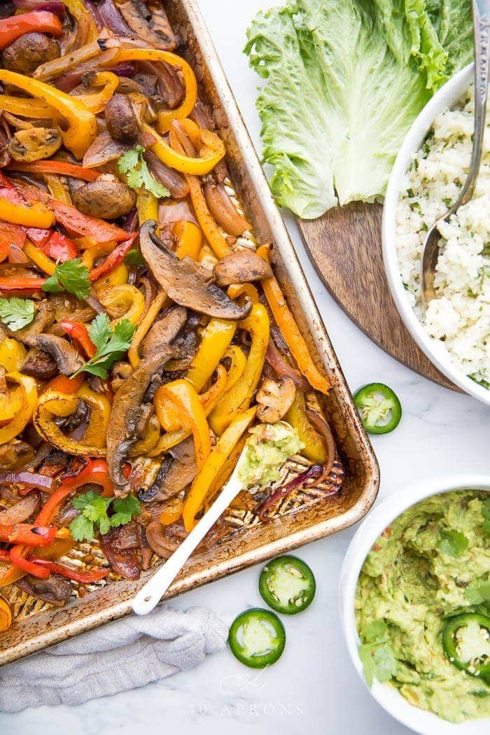 Overhead of Vegetarian sheet pan fajitas with a bowl of cauliflower rice and bowl of guacamole to the side