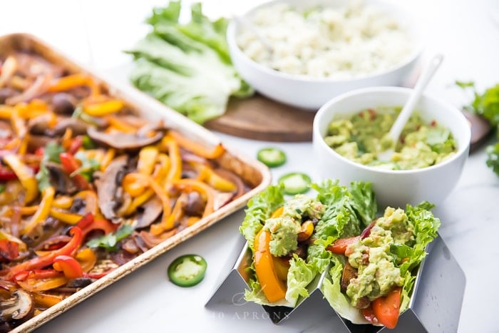 Vegetarian sheet pan fajitas in lettuce wraps next to the pan, a bowl of cauliflower rice, and bowl of guacamole