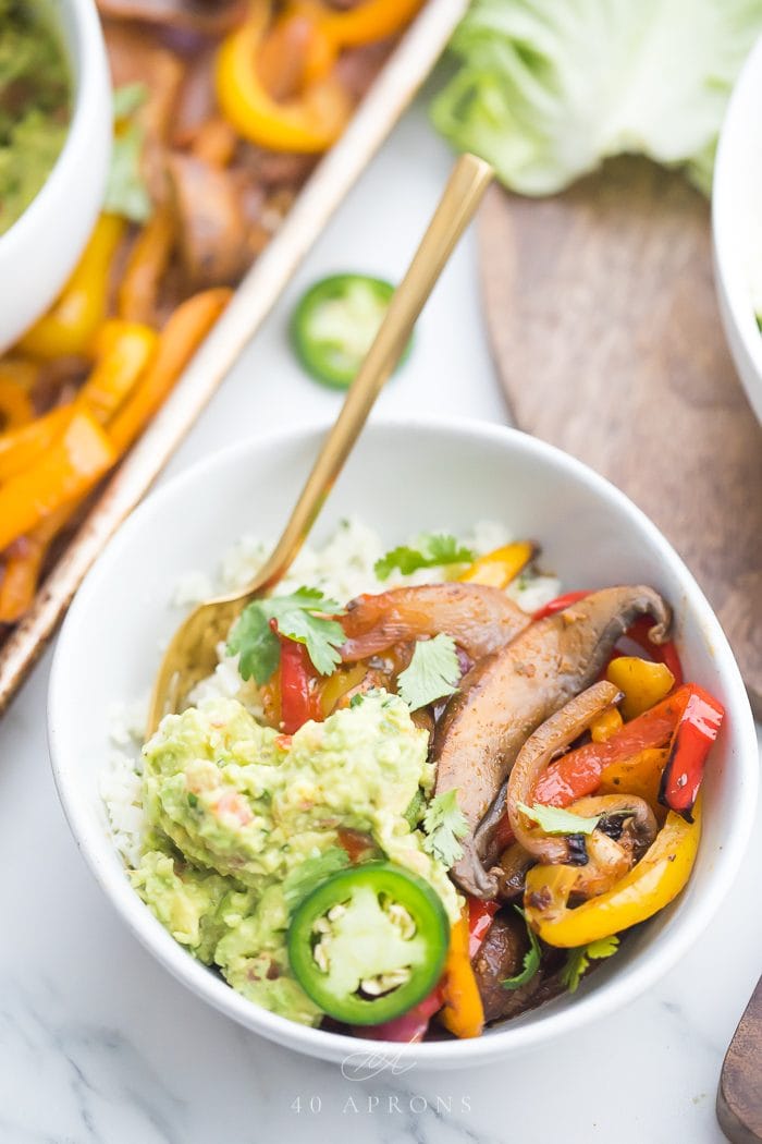 A burrito bowl made from sheet pan vegetarian fajitas topped with guacamole