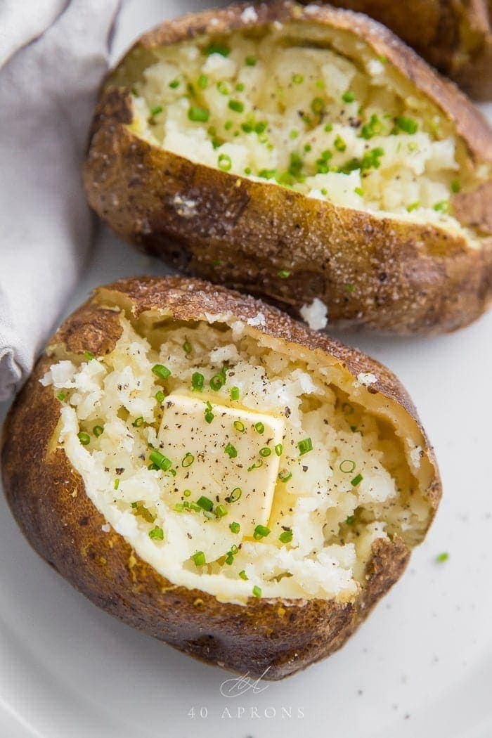 Baked potatoes from the grill on a plate open with pats of butter and chives