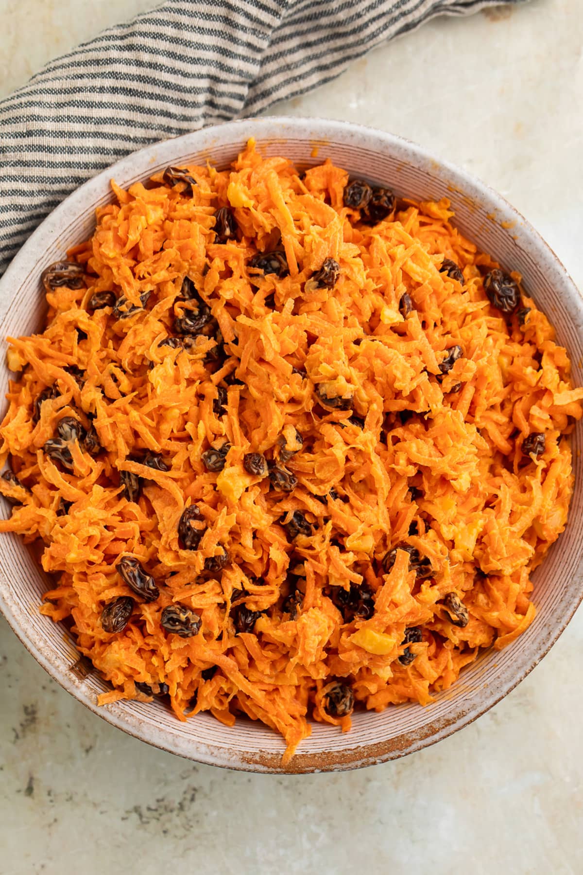 Overhead view of a bowl of carrot raisin salad on a table with a striped napkin.