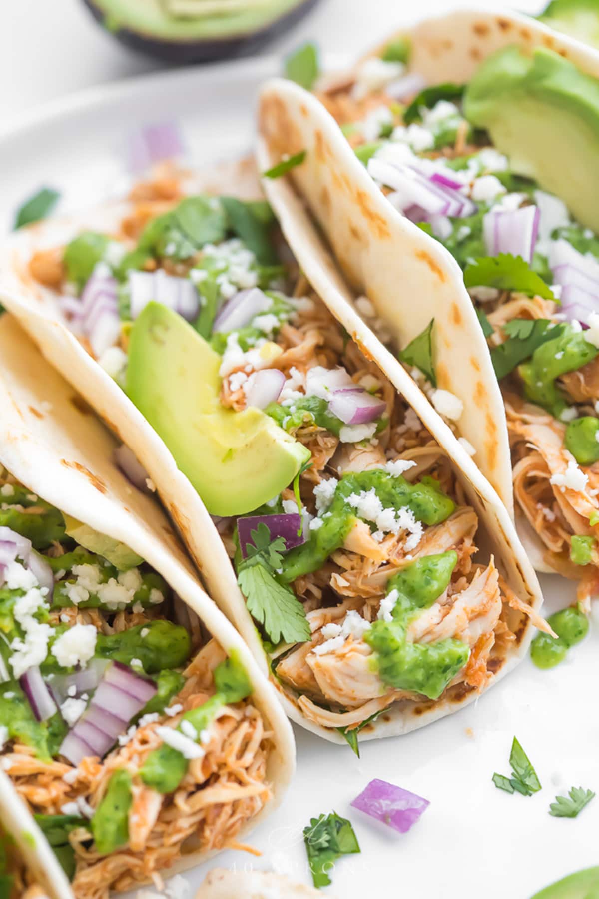 Close-up of Crockpot chicken tacos lined up in a row on a platter.