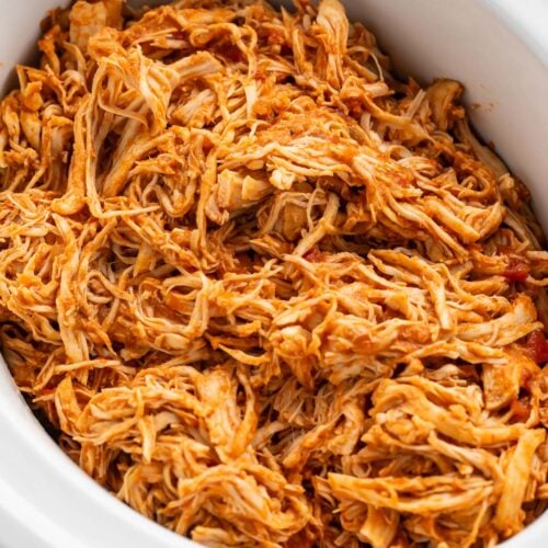 Shredded Mexican chicken in a white slow cooker on a kitchen counter.