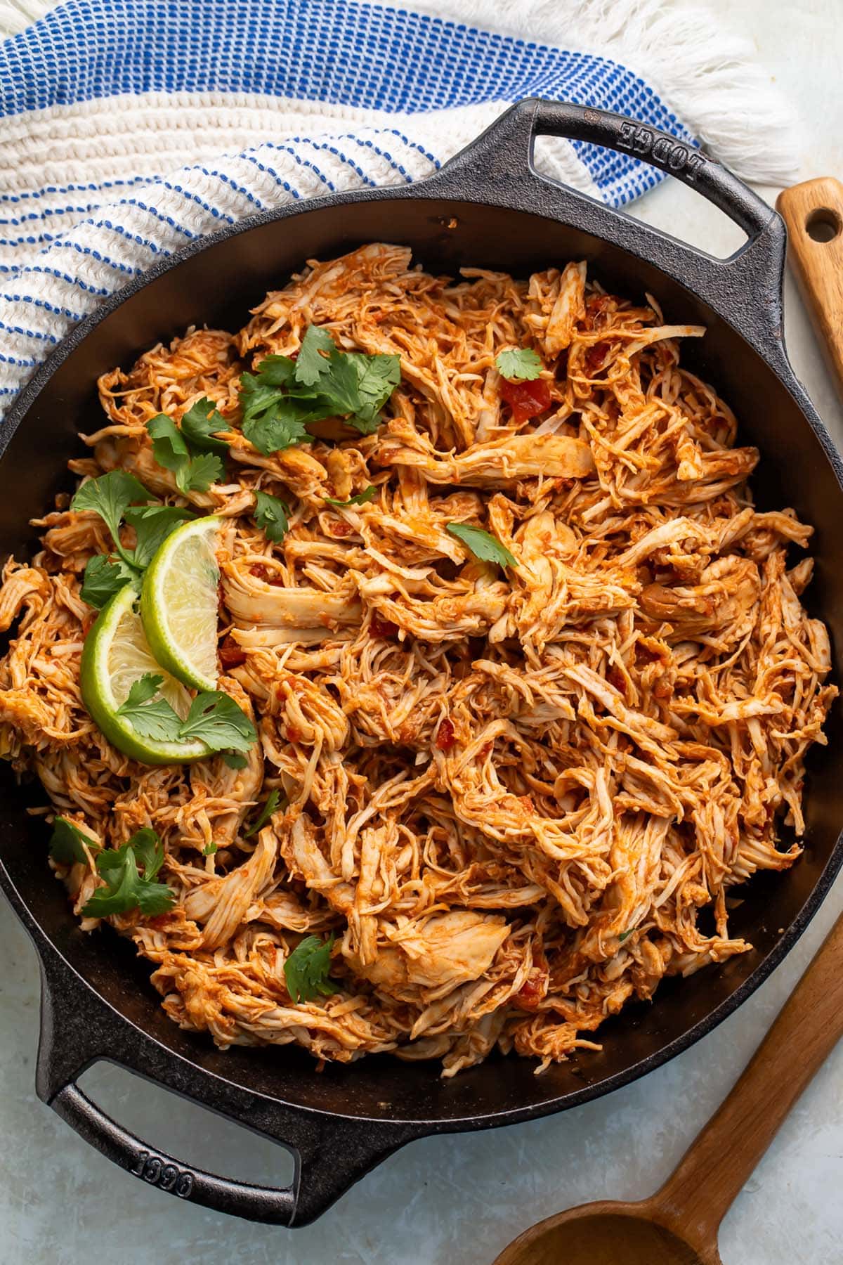 Slow cooker shredded Mexican chicken in a large cast-iron skillet, garnished with lime wedges and cilantro.