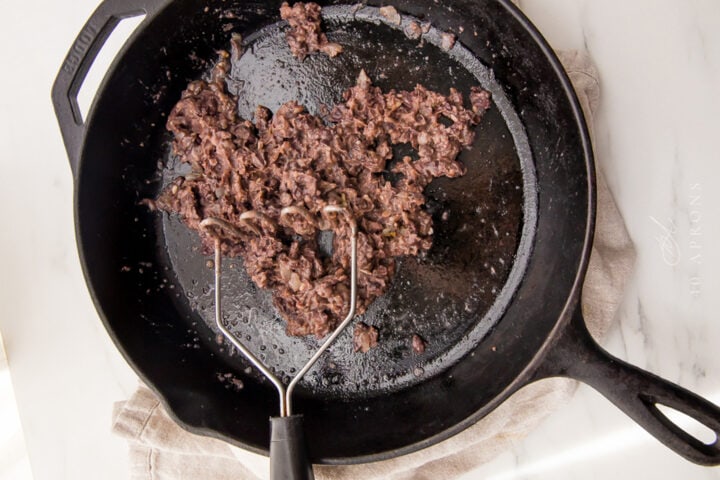 Mashed black beans in a large black cast-iron skillet.