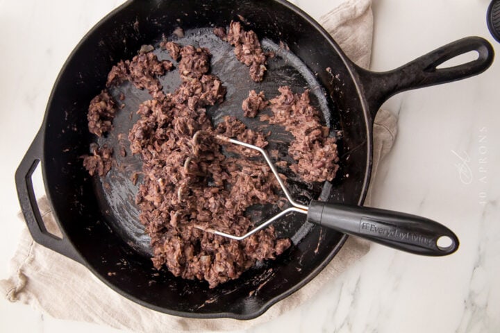 Mashed black beans in a large black cast-iron skillet.