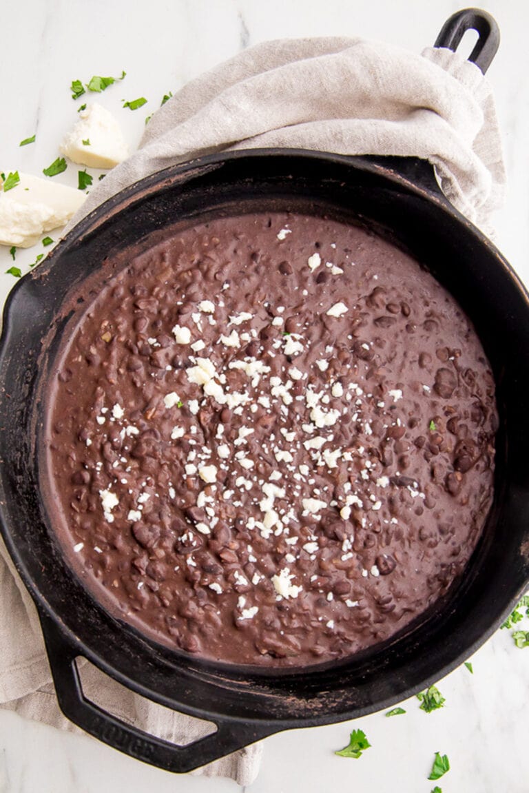 Refried black beans garnished with cotija crumbles in a large black cast iron skillet with a neutral cloth napkin around the handle.