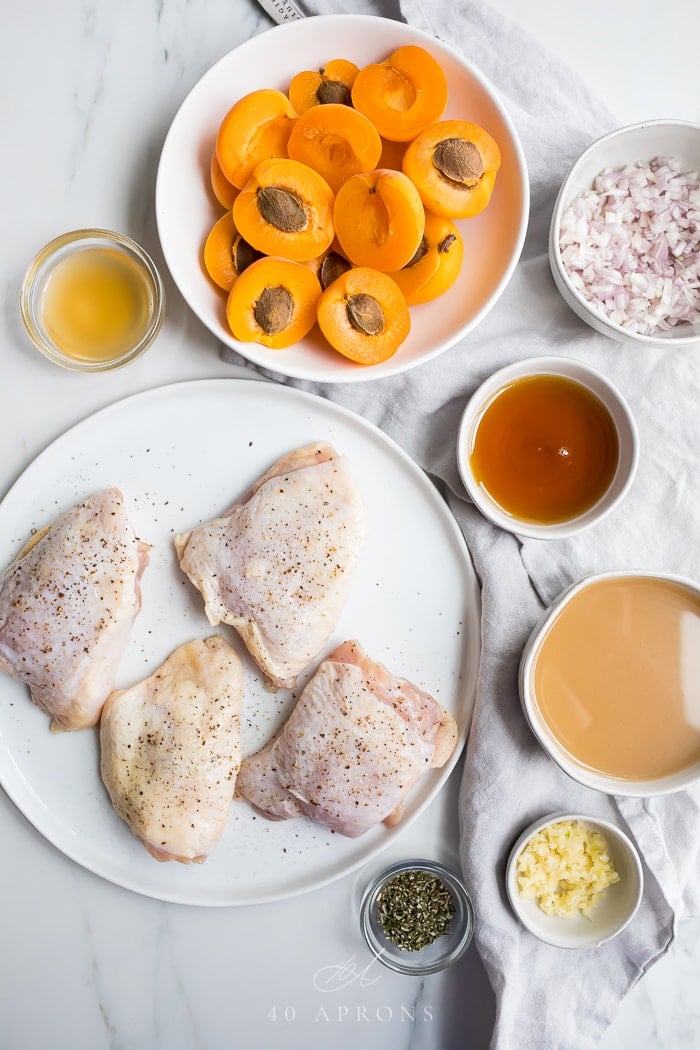 Seasoned chicken thighs on a white plate with prepped ingredients in white bowls