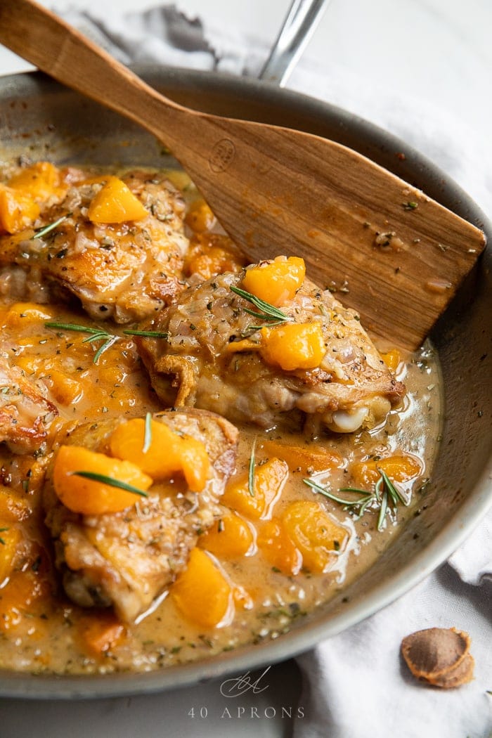 Apricot chicken in an ovenproof skillet with a wooden spoon