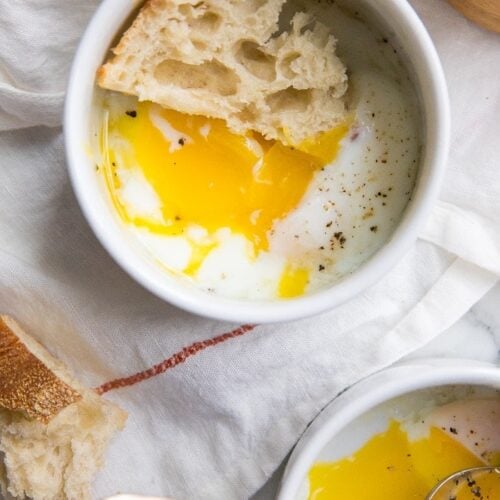 Sous vide eggs in small white bowls with crusty bread on top