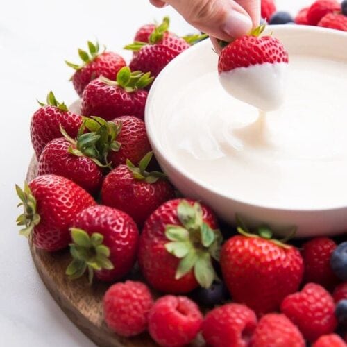 A bowl of yogurt fruit dip with a strawberry dipping in it