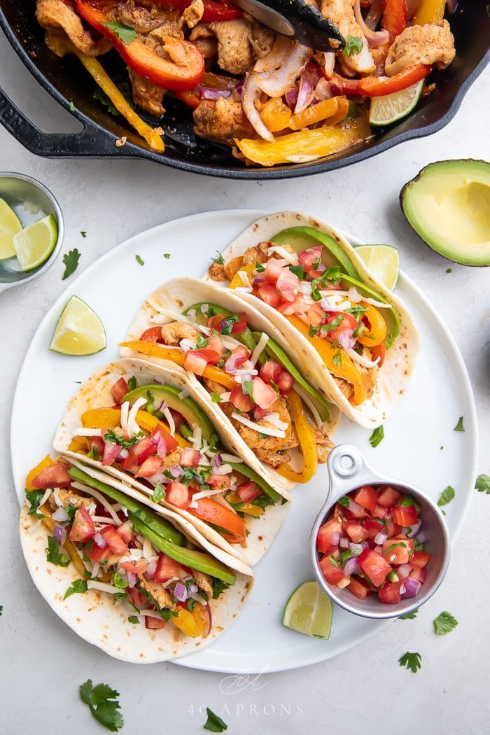 Crockpot chicken fajitas served in tortillas on a large white plate