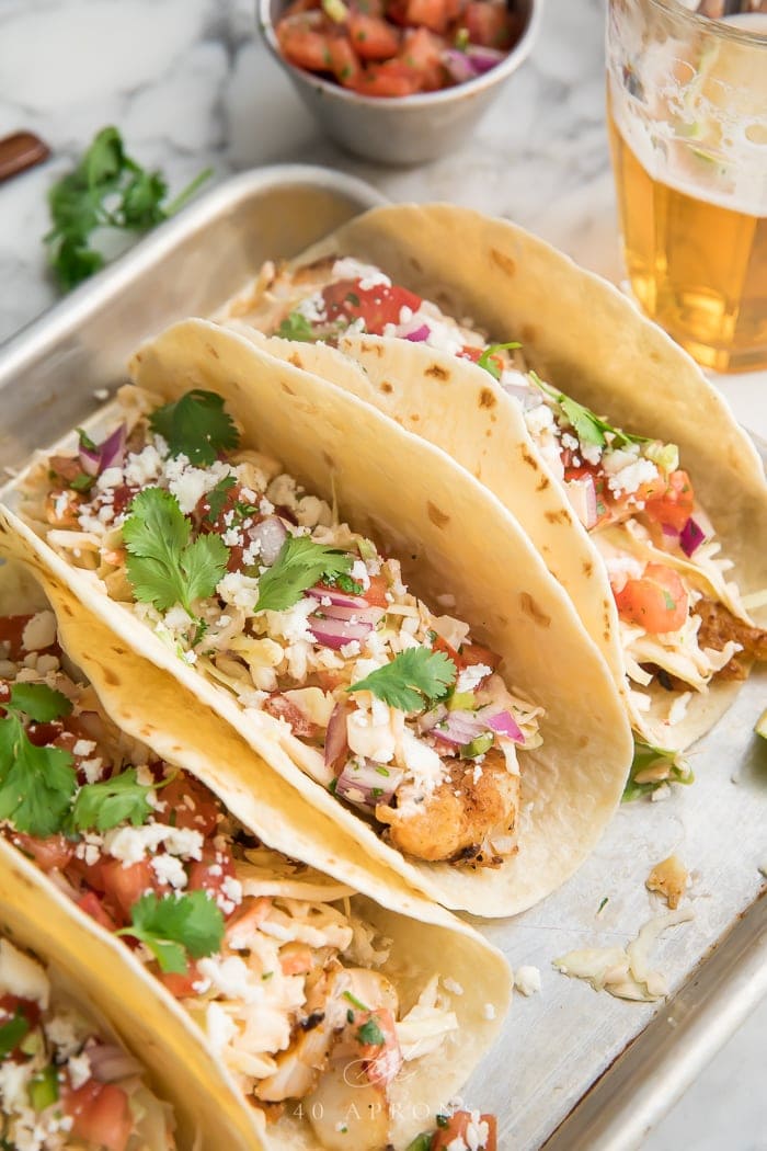 Three easy fish tacos on a metal tray with fresh herbs