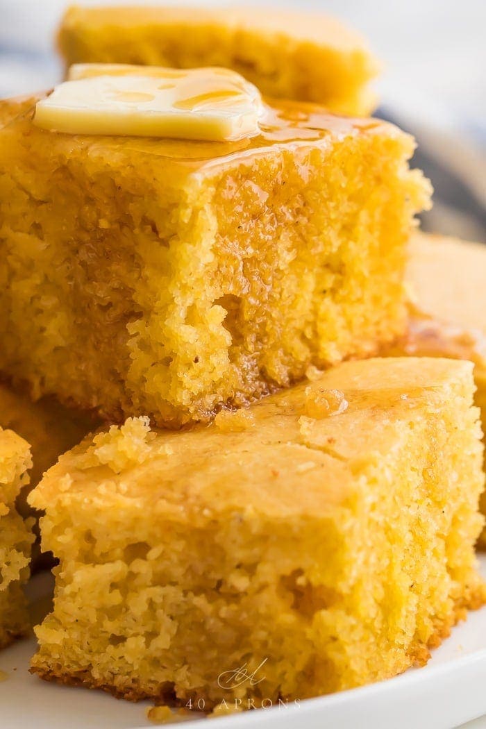 Gluten free cornbread stacked on a white plate with butter and honey