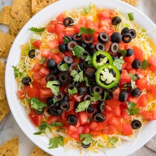 Taco dip in a white dish with tortilla chips around