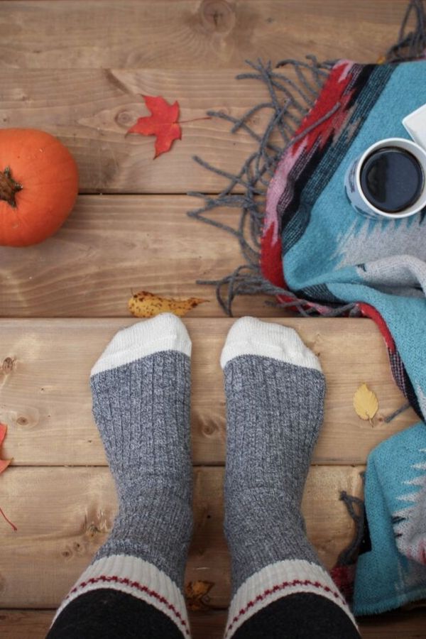 woman's feet in thick socks standing on a rustic wooden floor  between a pumpkin, a scarf and a mug of coffee 