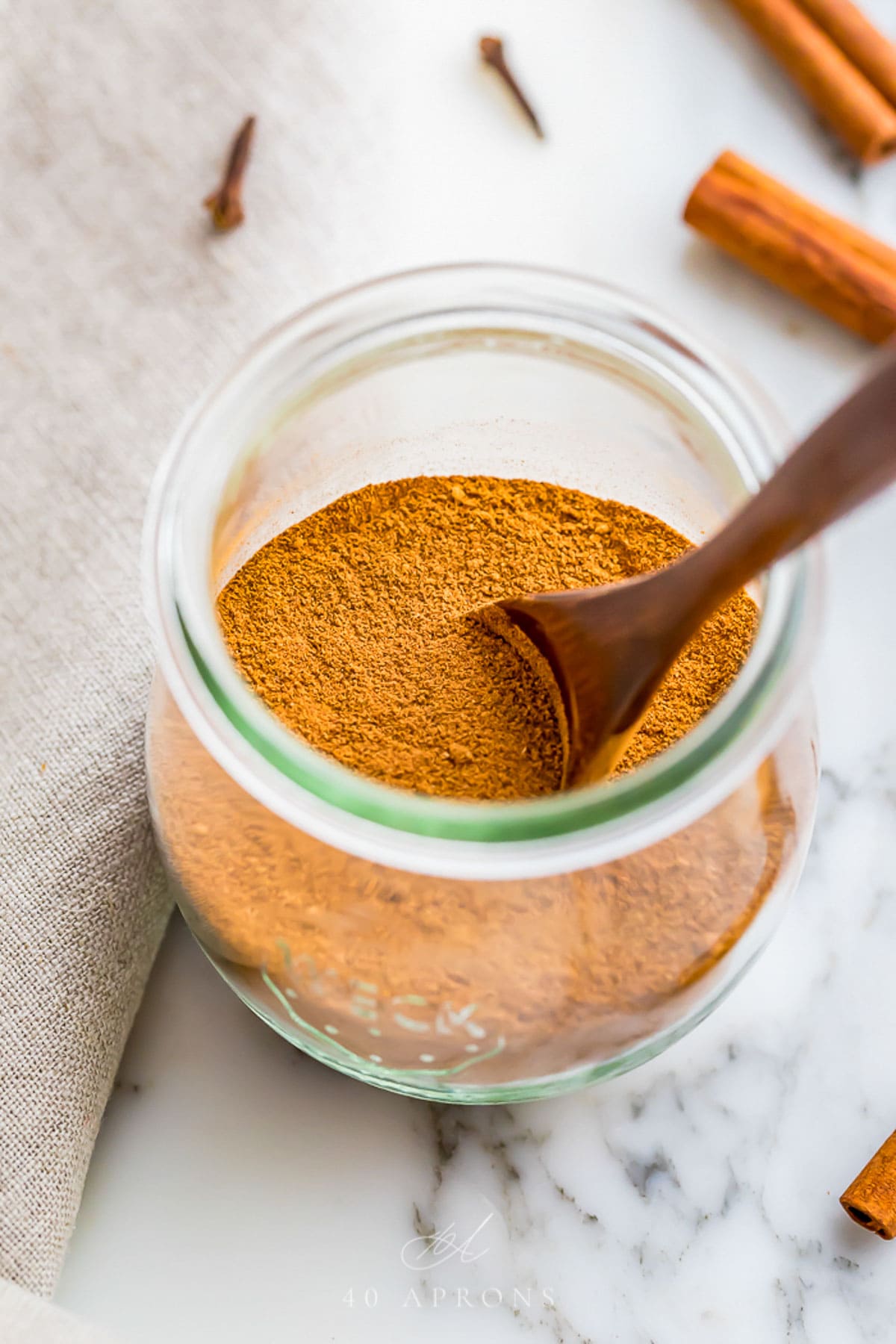 Homemade pumpkin pie spice blend in a glass jar with a wooden spoon.