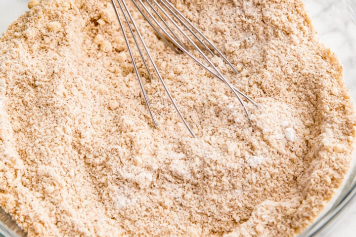 Dry ingredients for pumpkin muffins in a large glass mixing bowl with a silver whisk resting in the bowl.